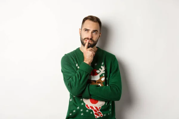 Nový rok oslavy a zimní prázdniny koncept. Pohledný vousatý muž plánuje Vánoce, přemýšlí a dívá se na levý horní roh, přemýšlí o dárkových nápadech, bílém pozadí — Stock fotografie