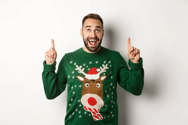 Kış tatili ve Noel. Komik süveter giyen heyecanlı sakallı adam, parmaklarıyla fotokopi alanını işaret ediyor, beyaz arka planda duruyor. — Stok fotoğraf