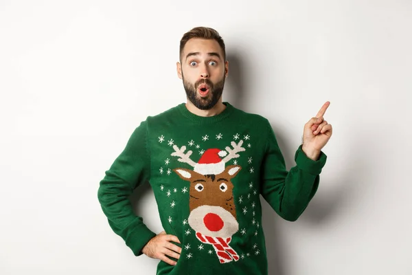 Zimní prázdniny a Vánoce. Muž vypadá vzrušeně jako ukazující prst přímo na logo, stojí ohromeně na bílém pozadí — Stock fotografie