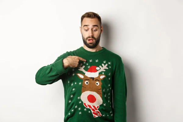 Kış tatili ve Noel. Süveter giymiş kafası karışmış bir adam kendini işaret ediyor, beyaz arka plan üzerinde şaşkın şaşkın duruyor. — Stok fotoğraf