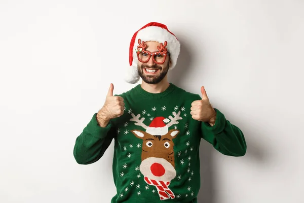 Feriados de Natal, conceito de celebração. Homem feliz em chapéu de Papai Noel e óculos de festa mostrando polegares para cima em aprovação, como algo, de pé sobre fundo branco — Fotografia de Stock