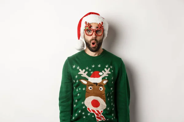 Noel tatili, kutlama konsepti. Noel Baba şapkalı ve parti gözlüklü bir adam beyaz arka planda duran harika bir şeye bakıyor. — Stok fotoğraf