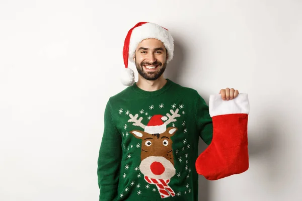 Vánoční večírek a sváteční koncept. Šťastný muž v Santa klobouk přináší dárky v vánoční ponožky a usmívá se, stojí nad bílým pozadím — Stock fotografie