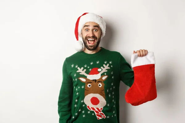 Xmas ve kış tatili konsepti. Mutlu adam Noel çorabında hediye aldı. Heyecanlı görünüyordu. Beyaz arka planda Noel Baba şapkası takıyordu. — Stok fotoğraf