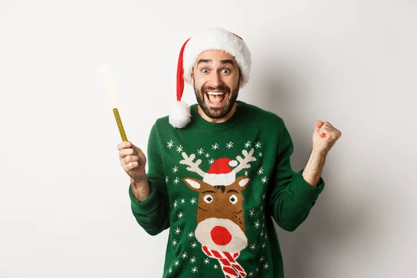 Noel partisi ve tatil konsepti. Yakışıklı, sakallı, neşeli, parti havai fişeği tutan, Noel Baba şapkası takan, yeni yılı kutlayan, beyaz bir geçmişi olan bir adam. — Stok fotoğraf