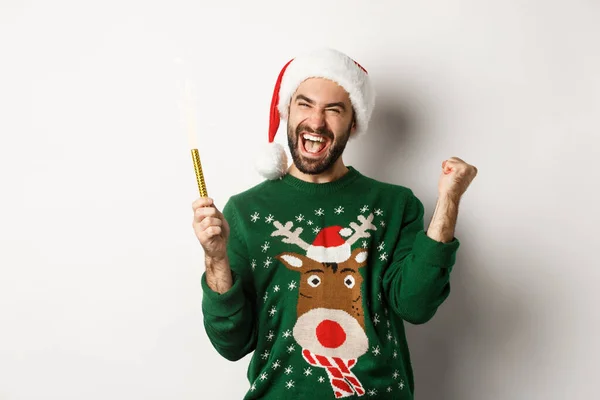 Vánoční večírek a sváteční koncept. Šťastný mladý muž slaví Nový rok, drží jiskru a vypadá nadšeně, stojí nad bílým pozadím — Stock fotografie