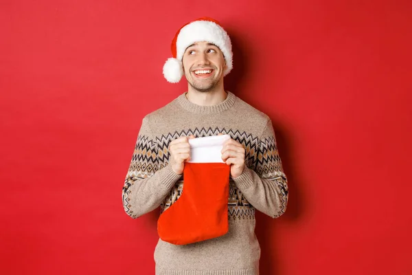 Concepto de vacaciones de invierno, año nuevo y celebración. Imagen del hombre sorprendido y feliz que recibe el regalo de santa secreta dentro de la bolsa de almacenamiento de Navidad, regalo abierto y buscando agradecido —  Fotos de Stock