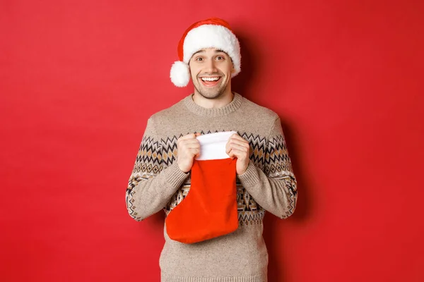 Koncept zimních prázdnin, Nový rok a oslavy. Obrázek překvapeného a šťastného muže, který dostává dárek od tajné Santa uvnitř vánoční punčocháče, otevřený dárek a vypadá vděčně — Stock fotografie