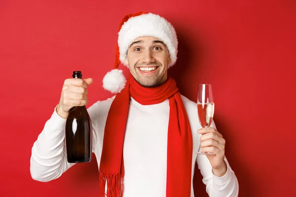 Begreppet vinter semester, jul och livsstil. Närbild av glada stilig man, håller champagne flaska och glas, gör rostat bröd för nytt år och firar, röd bakgrund — Stockfoto