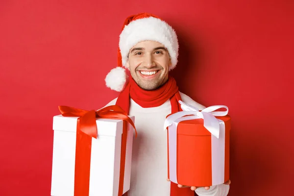 寒假、圣诞节和生活方式的概念。特写：笑容可亲、头戴圣诞礼帽、头戴围巾、笑容可亲的帅哥，祝新年快乐，还带着礼物，红着脸站在一旁 — 图库照片