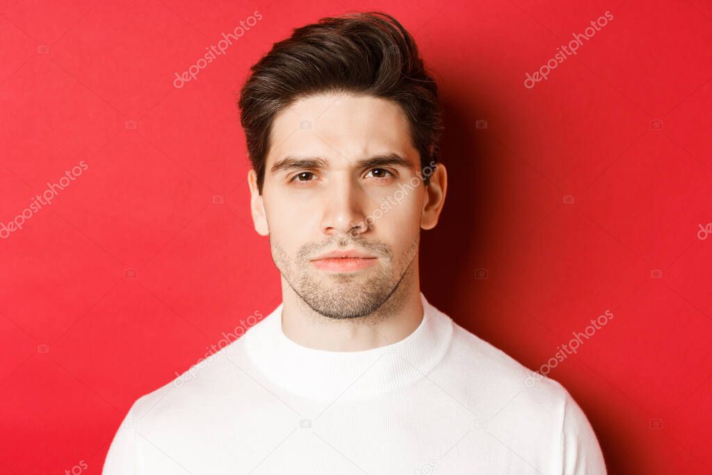 Close-up of thoughtful, serious-looking man in white sweater, standing over red background