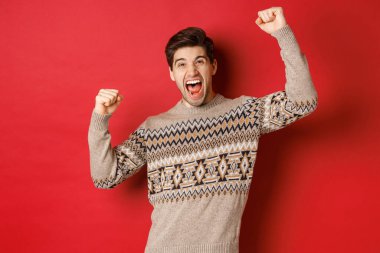 Noel arifesinde sevinen, el kaldıran, sevinç çığlıkları atan, kış tatillerini zaferle kutlayan, kırmızı arka planda duran yakışıklı bir adam.