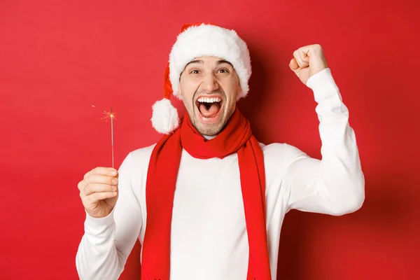 Begrip van Kerstmis, wintervakantie en viering. Portret van een opgewonden knappe man, hand omhoog steken en sterretje vasthouden, gelukkig nieuwjaar wensen, over rode achtergrond staan — Stockfoto