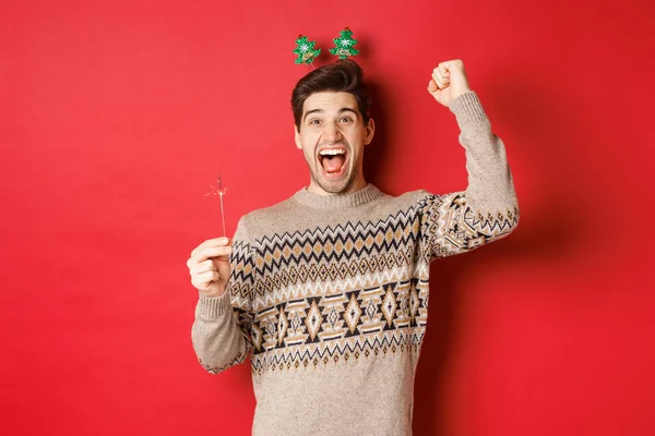 Cara alegre com um brilho regozijando e desejando feliz ano novo, levantando a mão para cima e gritando de alegria, de pé sobre fundo vermelho — Fotografia de Stock