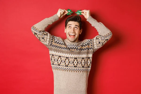 Koncept zimních prázdnin, vánoc a oslav. Obrázek legrační a roztomilý dospělý muž těší novoroční párty, usmívat se a radovat, stojící nad červeným pozadím — Stock fotografie