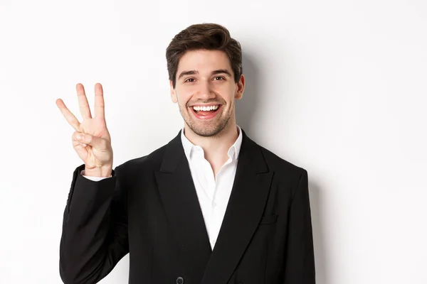 Nær en kjekk forretningsmann i svart dress, smilende, med nummer tre stående over hvit bakgrunn – stockfoto