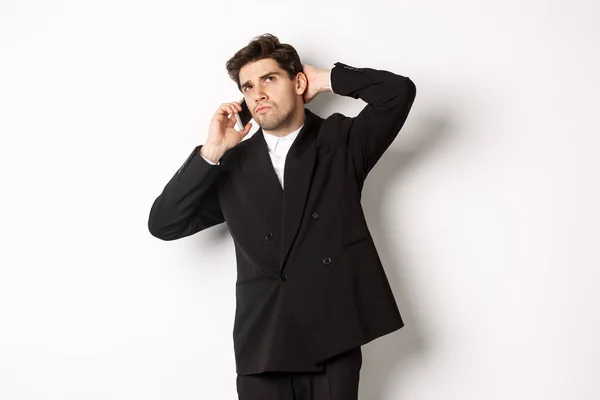 Image of indecisive businessman talking on phone and thinking, looking doubtful, making decision, standing over white background — Stock Photo, Image