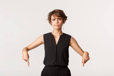 Şüpheci ve hayal kırıklığına uğramış genç bir kadın şikâyet ediyor, tatminsiz sırıtıyor ve parmaklarını aşağı işaret ediyor.