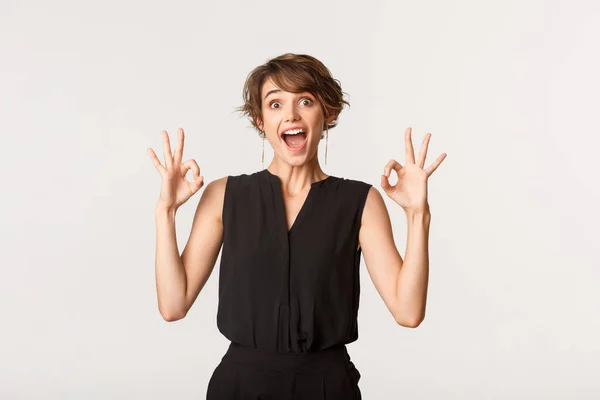 Stupito e impressionato giovane donna mostrando gesti ok con espressione affascinata, raccomandare il prodotto su sfondo bianco — Foto Stock