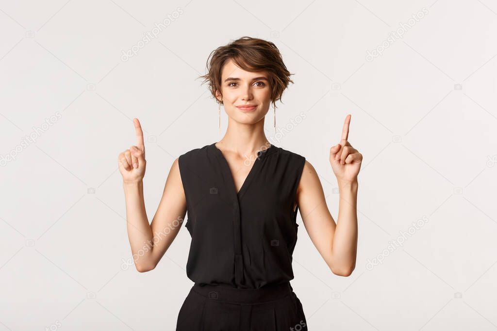 Image of confident attractive and stylish young woman pointing fingers up, showing logo, white background