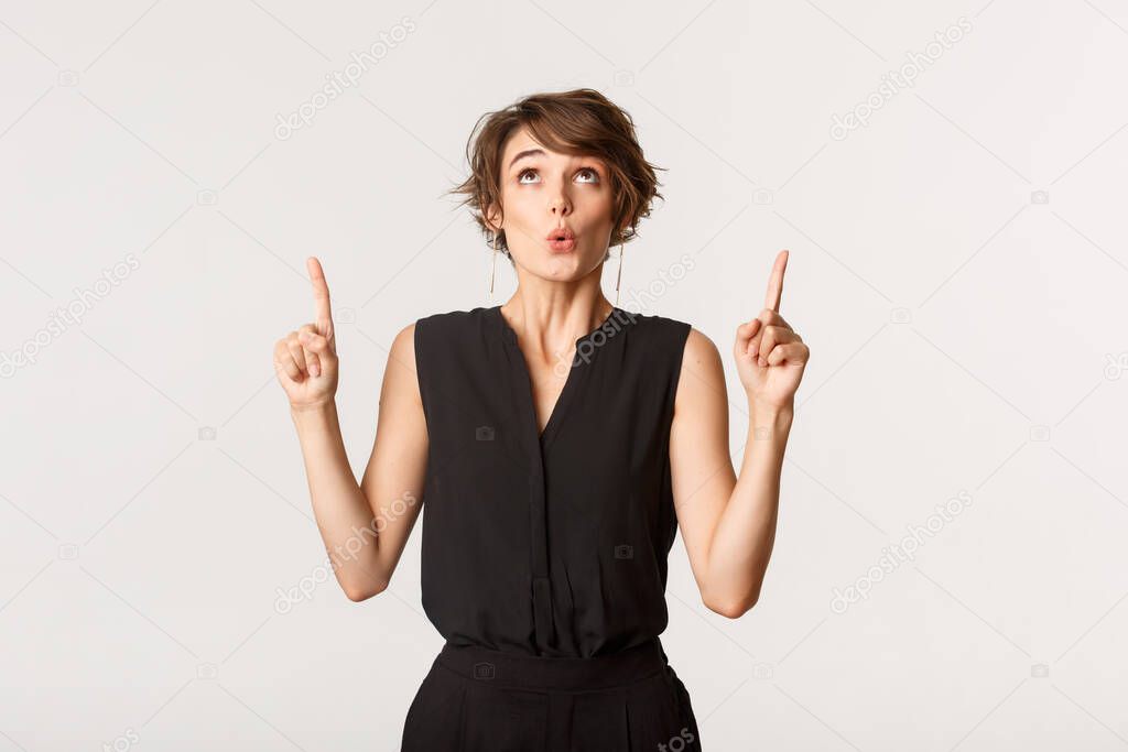 Image of surprised elegant lady in black outfit looking and pointing fingers up with wondered expression
