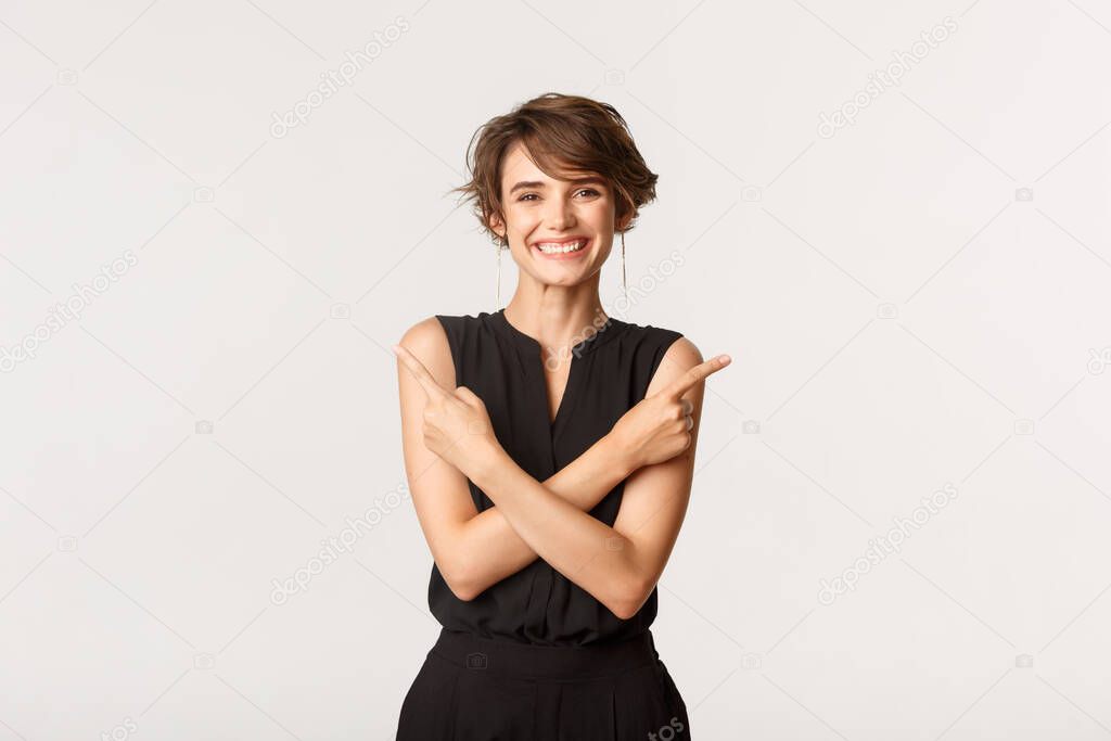 Cheerful attractive female smiling as pointing fingers sideways, showing two variants, making choice, standing white background