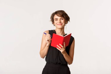 Gülümseyen çekici kadın not alıyor, çalışma saatlerini not alıyor, beyaz arka planda duruyor.