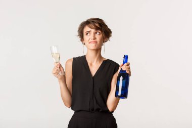 Kuşkucu ve cahil genç bir kadın rahatsız, berbat bir partide şampanya içiyor, beyaz arka planda dikiliyor.