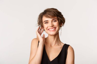 Kameraya gülümseyen, beyaz arka planda duran zarif ve çekici bir kadının yakın çekimi.