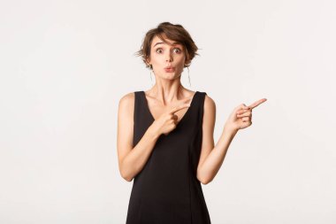 Meraklı bir kızın, kameraya bakıp, beyaz arka planda duran ürünleri işaret etmesi.