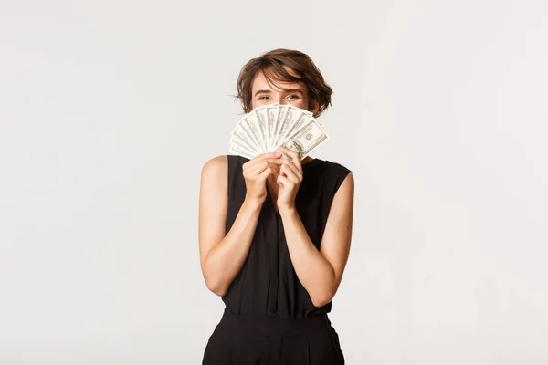 Glada lycklig flicka som håller pengar över ansiktet och ler, står över vit bakgrund — Stockfoto