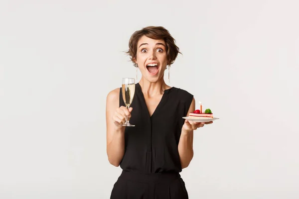 Image of young amazed woman attend birthday celebration party, holding glass of champagne and cake — Stock Photo, Image