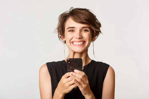 Close-up de mulher feliz segurando smartphone, sorrindo para a câmera, de pé sobre fundo branco — Fotografia de Stock