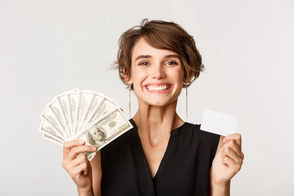 Närbild av framgångsrika affärskvinna leende, visar kreditkort och pengar, står över vit bakgrund — Stockfoto