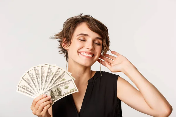 Bekymmerslös elegant rik kvinna ler, visar pengar, står över vit bakgrund — Stockfoto