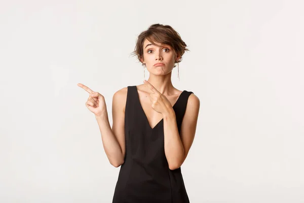 Imagen de una chica insegura haciendo pucheros mirando a la izquierda con expresión indecisa, de pie sobre fondo blanco — Foto de Stock