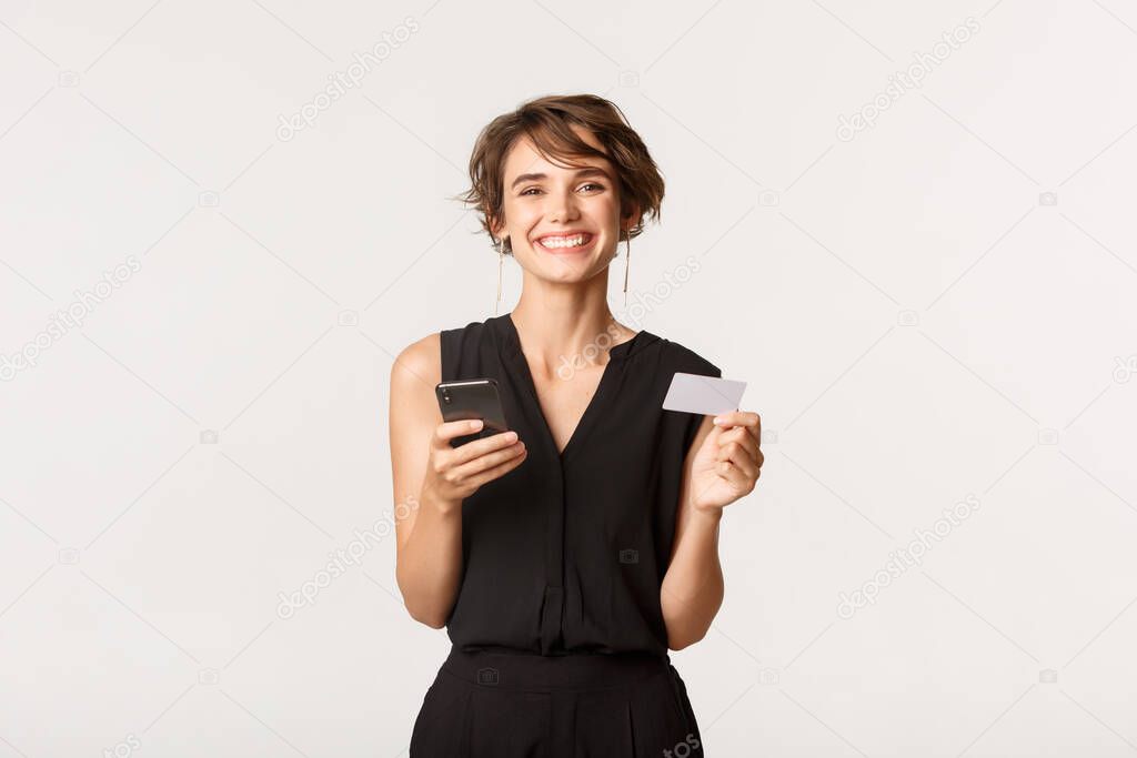 Cheerful beautiful female with credit card and smartphone smiling at camera