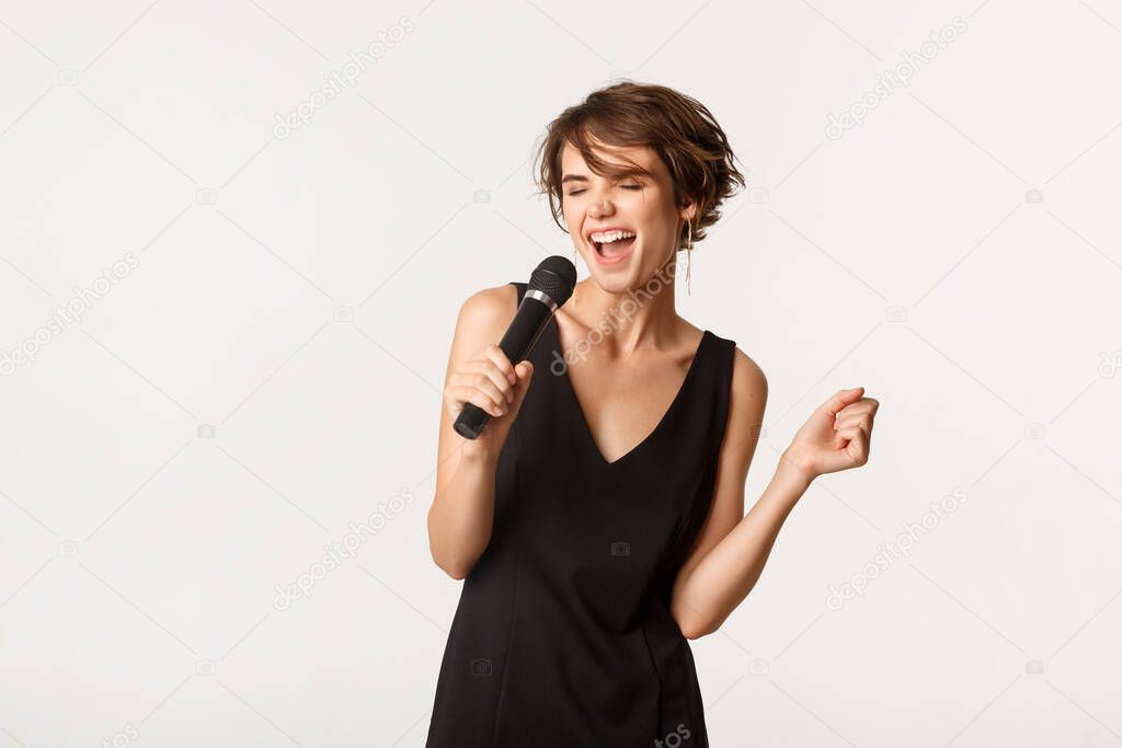 Attractive stylish woman singing song in microphone, performing over white background