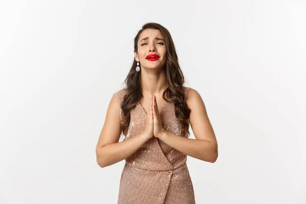 Celebración y concepto de fiesta. Mujer desesperada en vestido de glamour rogando por algo, necesita ayuda y de la mano en la oración, llorando y suplicando, de pie sobre fondo blanco —  Fotos de Stock