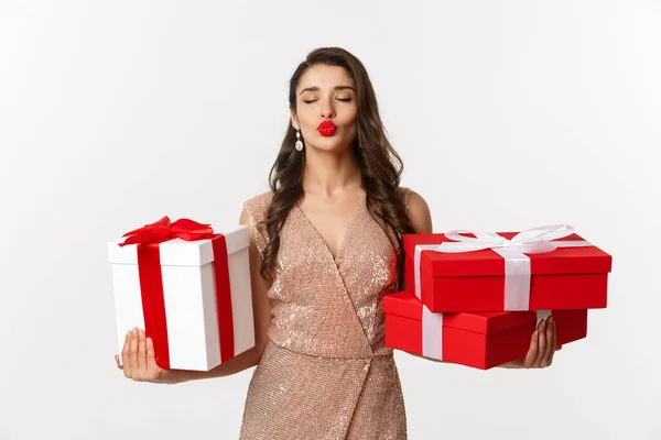 Vacaciones, concepto de celebración. Hermosa mujer caucásica en vestido elegante sosteniendo regalos de Navidad y sonriendo feliz, de pie sobre fondo blanco — Foto de Stock