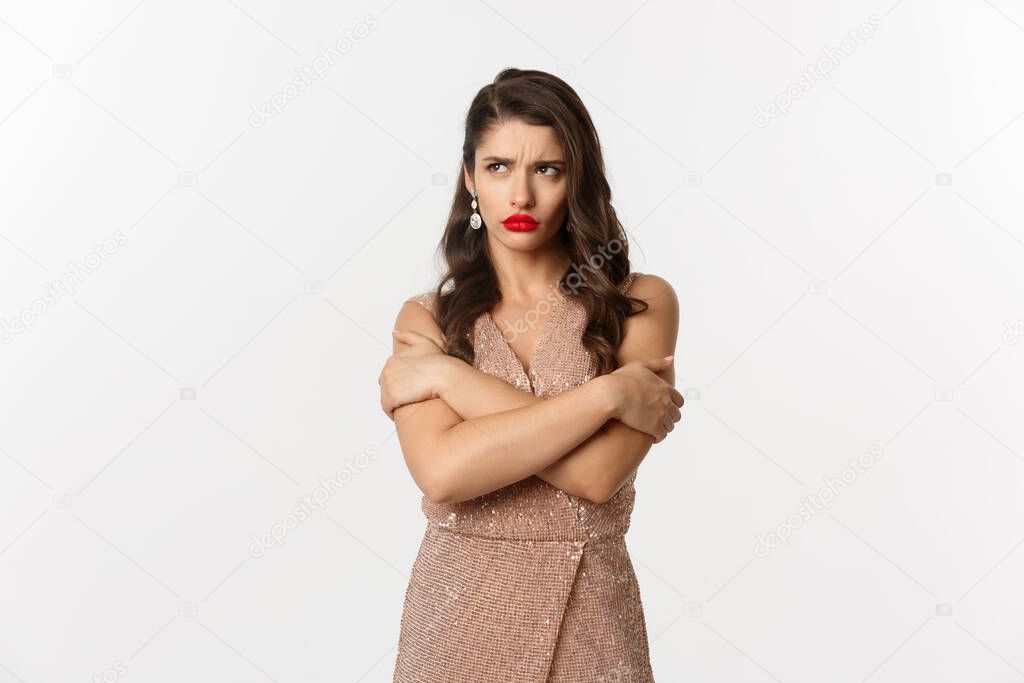 Celebration and party concept. Sulking woman looking angry, dressed for formal event in glamour dress, hugging herself and pouting upset, white background