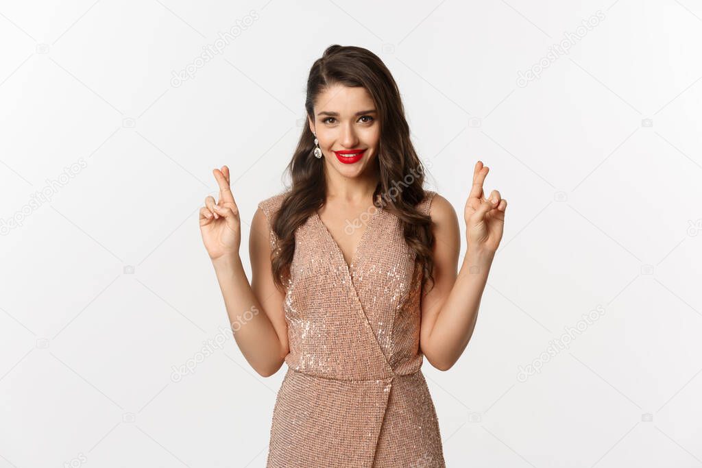 Concept of casino, celebration and party. Hopeful beautiful woman making a wish, cross fingers for good luck and looking confident, white background
