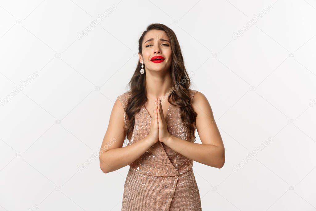 Celebration and party concept. Desperate woman in glamour dress begging for something, need help and holding hands in pray, crying and pleading you, standing over white background