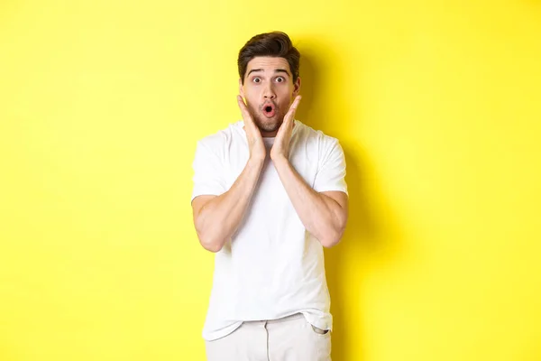 Imaginea unui bărbat chipeș care arată surprins, trăgând și spunând wow, uitându-se la oferta promoțională uimită, stând deasupra fundalului galben — Fotografie, imagine de stoc