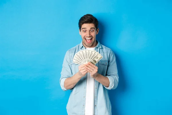 Emocionado hombre exitoso contando dinero, mirando satisfecho en efectivo y sonriendo, de pie sobre fondo azul — Foto de Stock