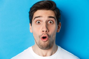 Şaşırmış bir adamın görüntüsü hayret verici ve hayret verici bir şekilde kameraya bakıp mavi arka planda dikildiğini merak ediyordu.