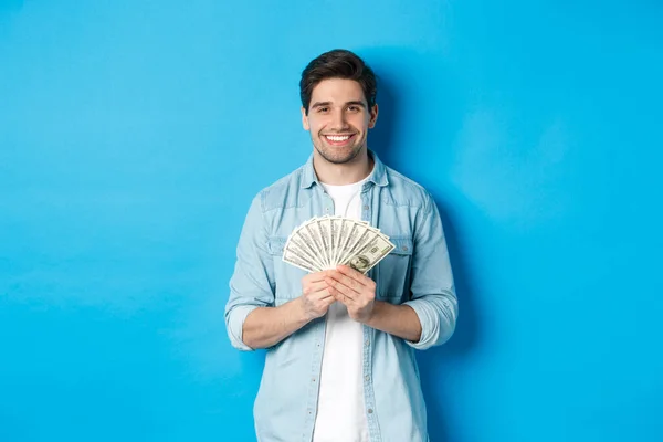 Hombre sonriente guapo sosteniendo dinero, concepto de finanzas y banca, de pie sobre fondo azul — Foto de Stock