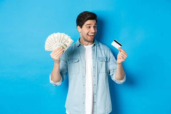 Sorprendido y feliz hombre mirando a la tarjeta de crédito y mostrando dinero, concepto de préstamo bancario, finanzas e ingresos. — Foto de Stock