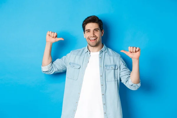Portrait of confident man pointing at himself, being a professional, bragging while standing against blue background — Stock Photo, Image