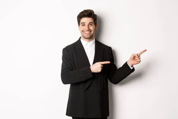 Image of attractive smiling guy dressed for new year party, pointing fingers right and showing advertisement, standing over white background — Stock Photo, Image